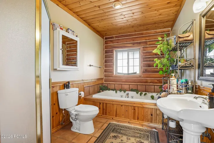 A soaking tub set in a wood surround with a pedestal sink alongside. The right way to close out a long day on the mountain.A soaking tub set in a wood surround with a pedestal sink alongside. The right way to close out a long day on the mountain.Full bathroom with a soaking tub set in a wood surround, pedestal sink, wood wainscoting, and a window.