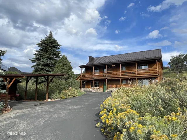 The circular driveway means no backing down the hill, and the covered carport keeps a vehicle out of the snow. Mature pines and native rabbitbrush line the drive.