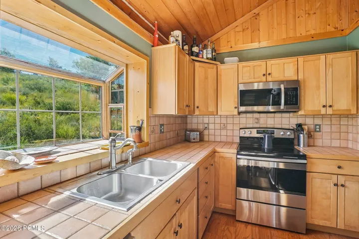 Eat-in kitchen with a stainless electric range, tile counters, wood cabinets, and a picture window looking out to the hillside.Eat-in kitchen with a stainless electric range, tile counters, wood cabinets, and a picture window looking out to the hillside.Kitchen with a stainless electric range, tile countertops, wood cabinets, and a picture window over the sink.