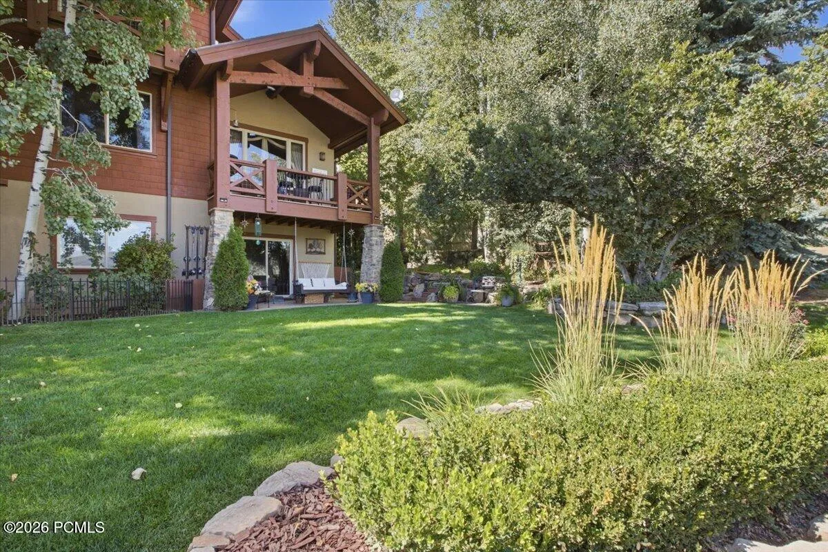 Expansive green lawn with established landscaping, a multi-level deck, and a lower patio with sliding glass doors