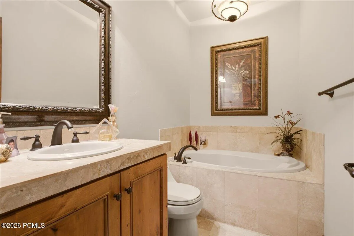 Built-in jetted tub with tile surround, wood-finish vanity with an oval sink, and a framed mirror