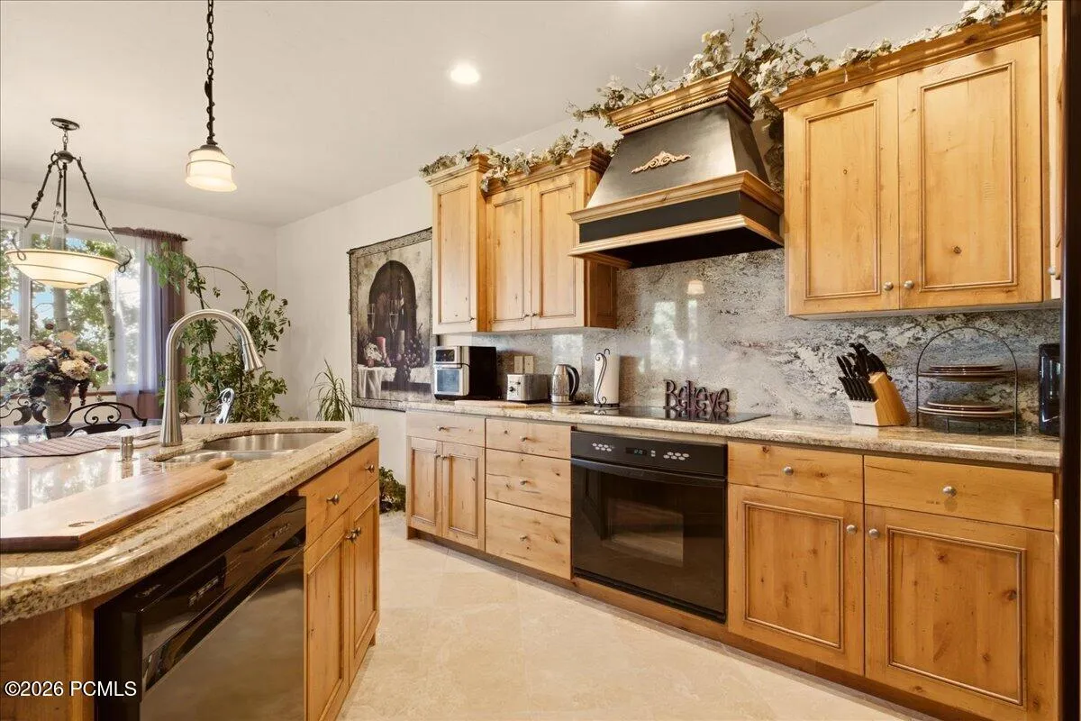 Kitchen featuring wood cabinetry, granite countertops, built-in dishwasher, and travertine floors