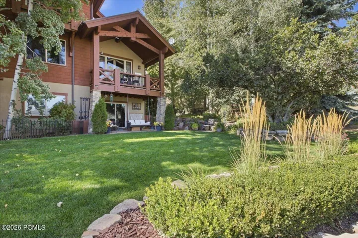 Expansive green lawn with established landscaping, a multi-level deck, and a lower patio with sliding glass doors