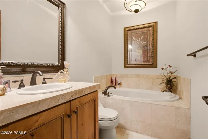 Built-in jetted tub with tile surround, wood-finish vanity with an oval sink, and a framed mirror