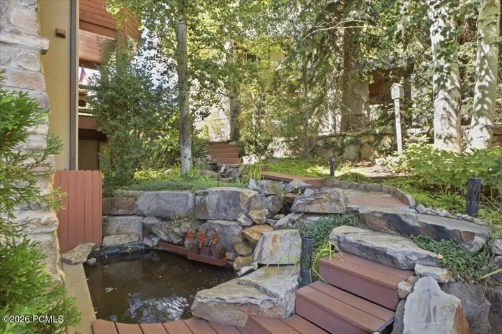 Water feature with natural stone and tiered landscaping, wood-finish decking, and mature trees