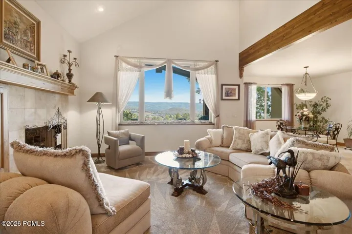 Vaulted ceilings with exposed wood beams, fireplace with a mantel, and large windows showcasing the view of the valley
