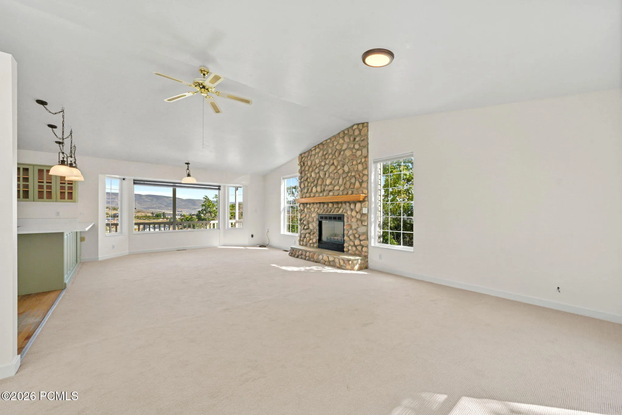 Spacious room featuring a stone-clad fireplace with a wood mantel, multiple large windows, and a built-in wet bar with cabinetry