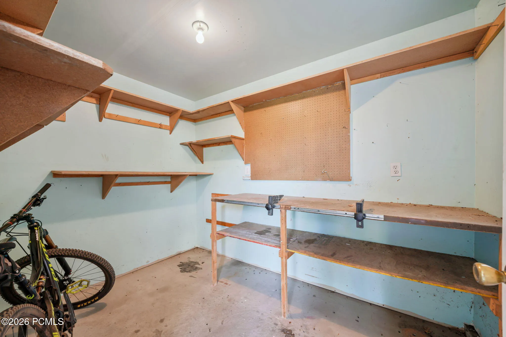 Built-in shelving, pegboard, concrete flooring, and a workbench with integrated vises connected to garage