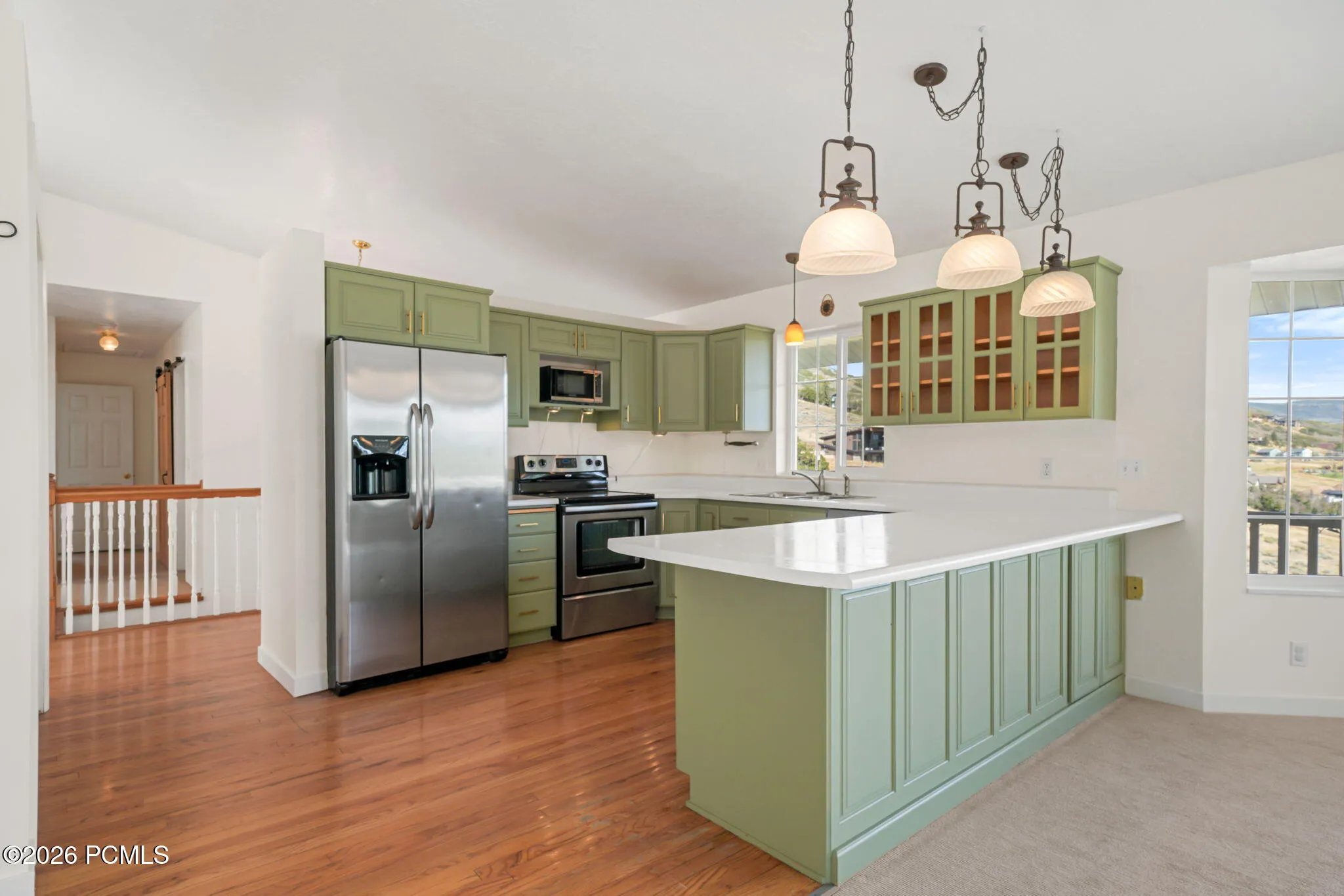 Kitchen with wood-finish flooring, green cabinetry, white countertops, and stainless steel appliances
