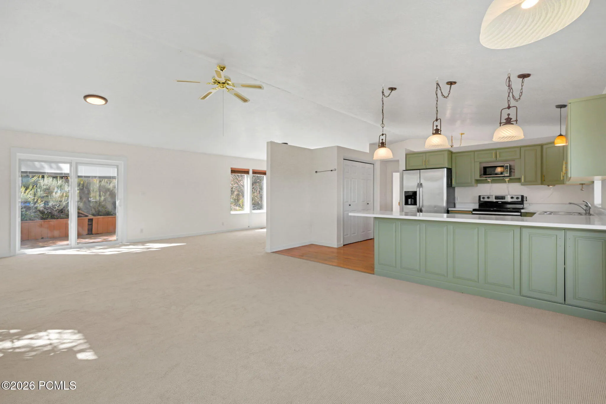 Open-concept living space with sliding glass doors, ceiling fan, and carpet flooring