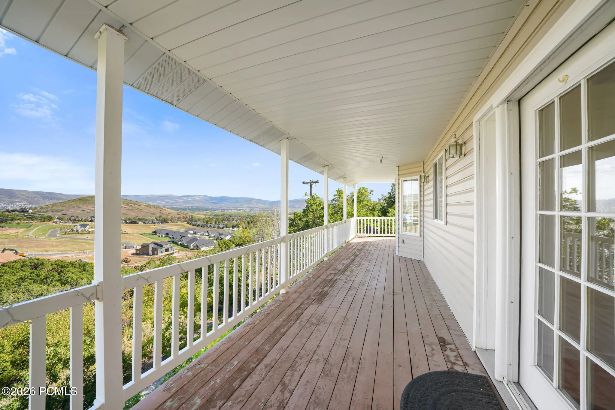Expansive covered deck with wood-finish flooring, white railing, and multiple support columns