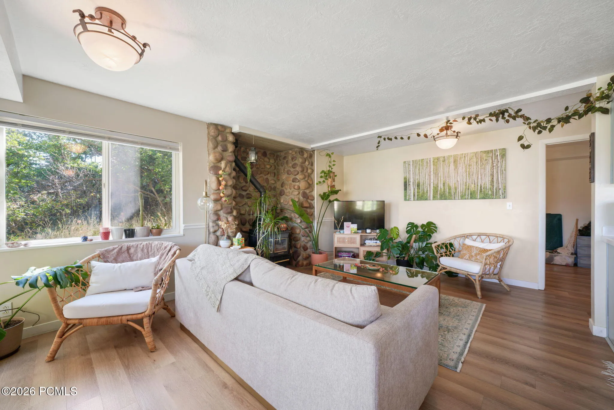 Light wood-finish flooring, stone-clad fireplace, white window trim, and semi-flush mount lighting fixtures