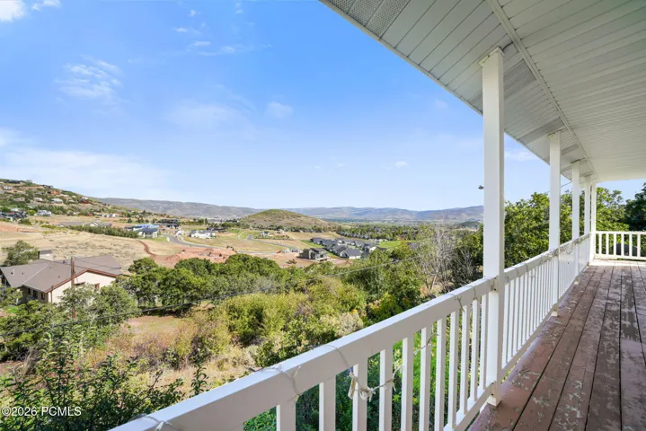 Expansive covered deck with wood flooring and white railing, featuring distant mountain scenery and surrounding properties