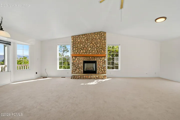 Vaulted ceiling, large windows, stone fireplace with wood mantel, and carpeting