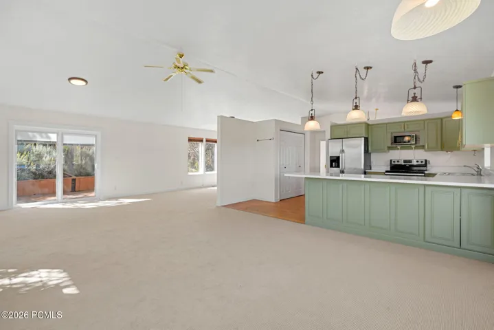 Open-concept living space with sliding glass doors, ceiling fan, and carpet flooring