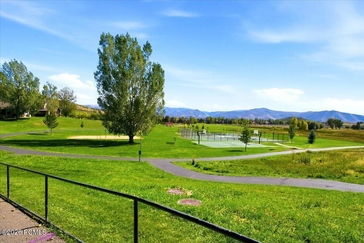 Expansive green space featuring a paved path, mature trees, and a multi-sport court