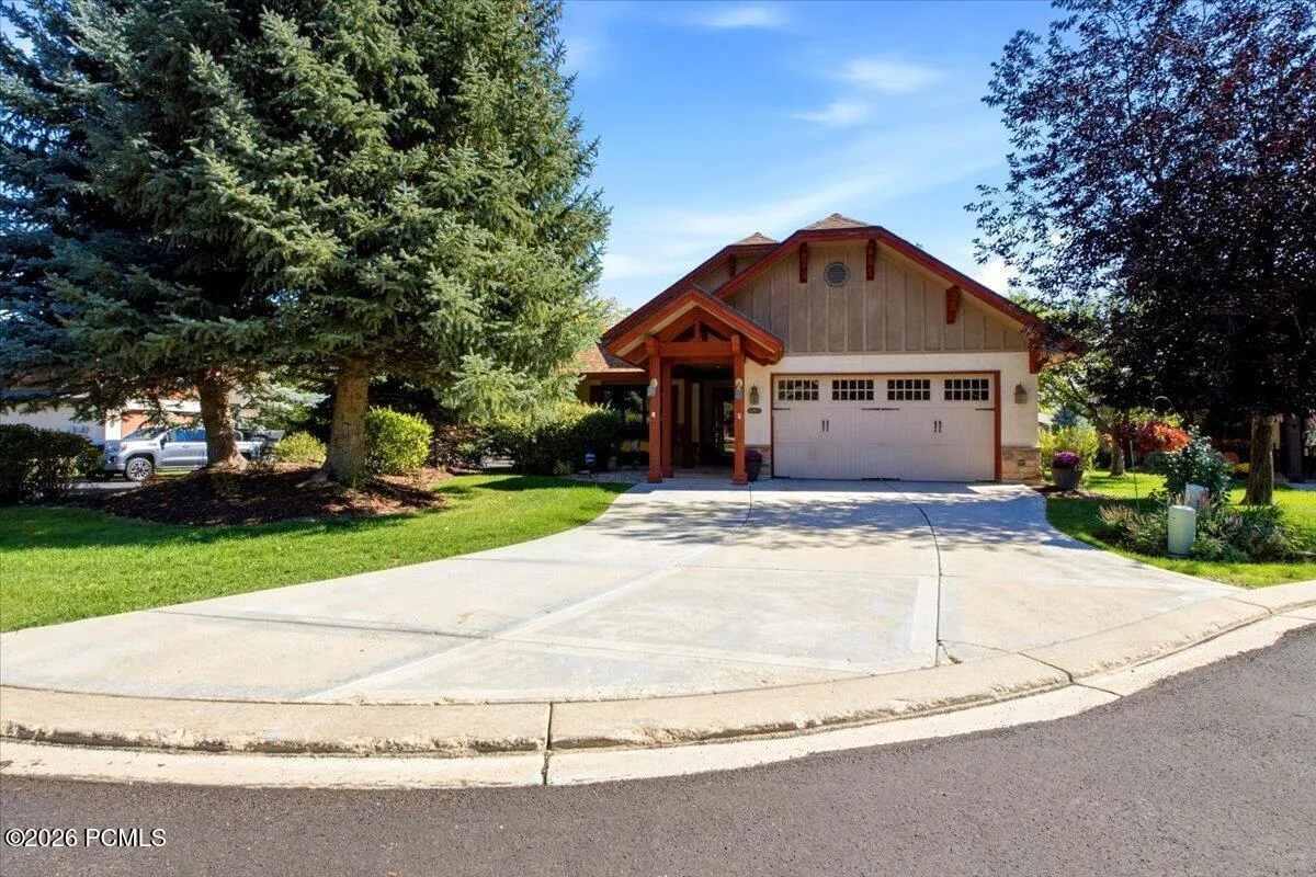 Front of home featuring an attached two-car garage, spacious concrete driveway, and mature trees