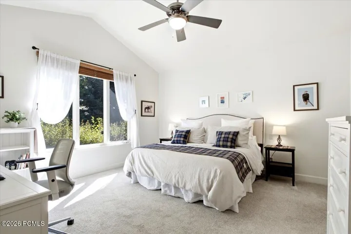 Primary suite featuring a vaulted ceiling, ceiling fan, and a large window