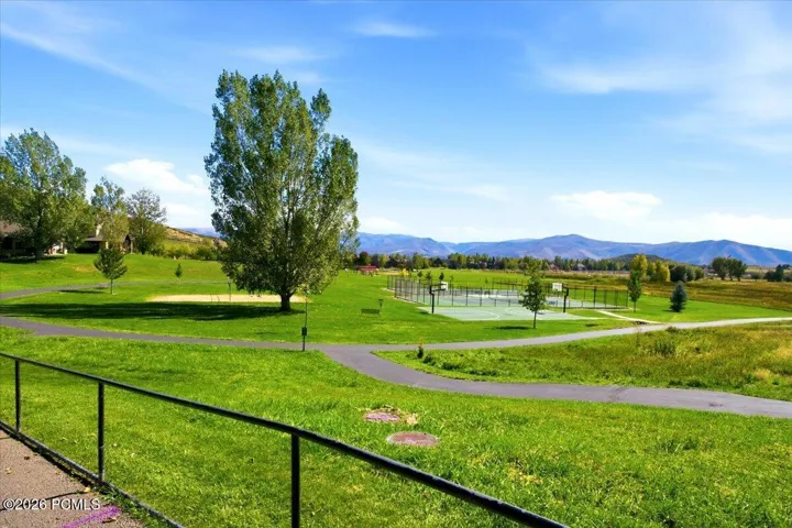 Expansive green space featuring a paved path, mature trees, and a multi-sport court