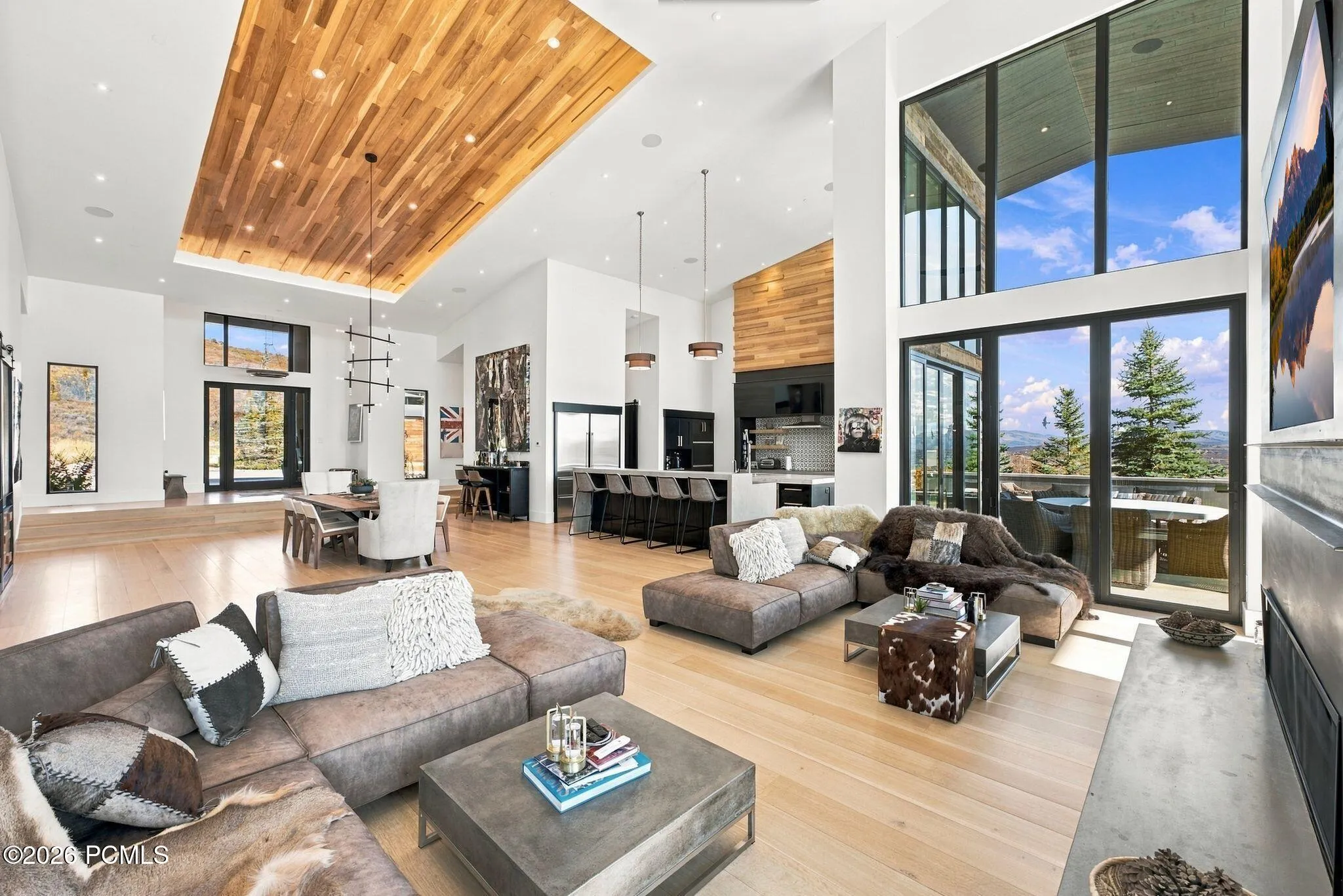 Expansive interior featuring floor-to-ceiling windows, wood-finish flooring, a kitchen island with stone countertops, a coffered wood-paneled ceiling, and sliding glass doors