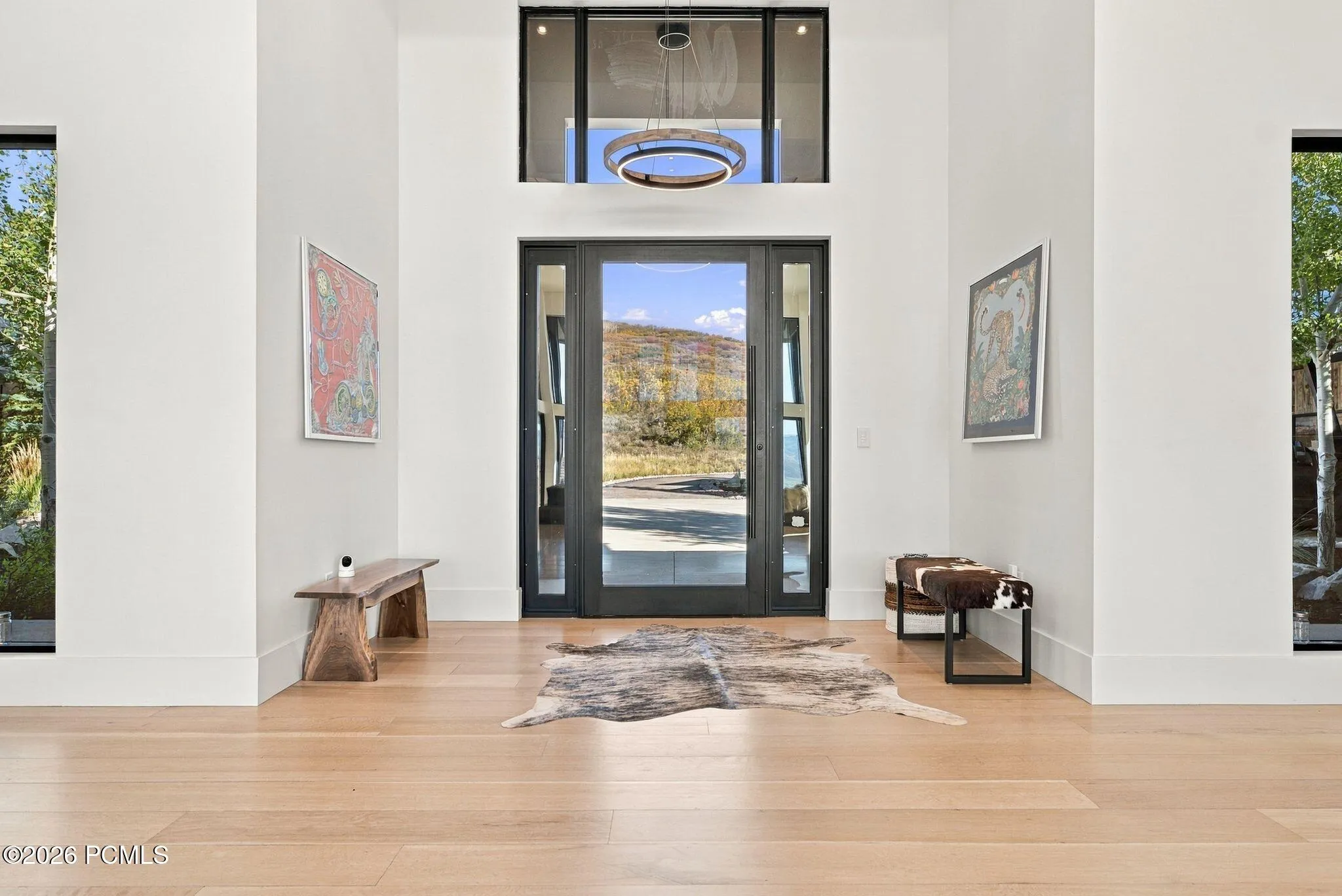 Grand entryway featuring double-height ceilings, a floor-to-ceiling glass-paneled front door with flanking sidelights, a large transom window, and wide-plank wood-finish flooring