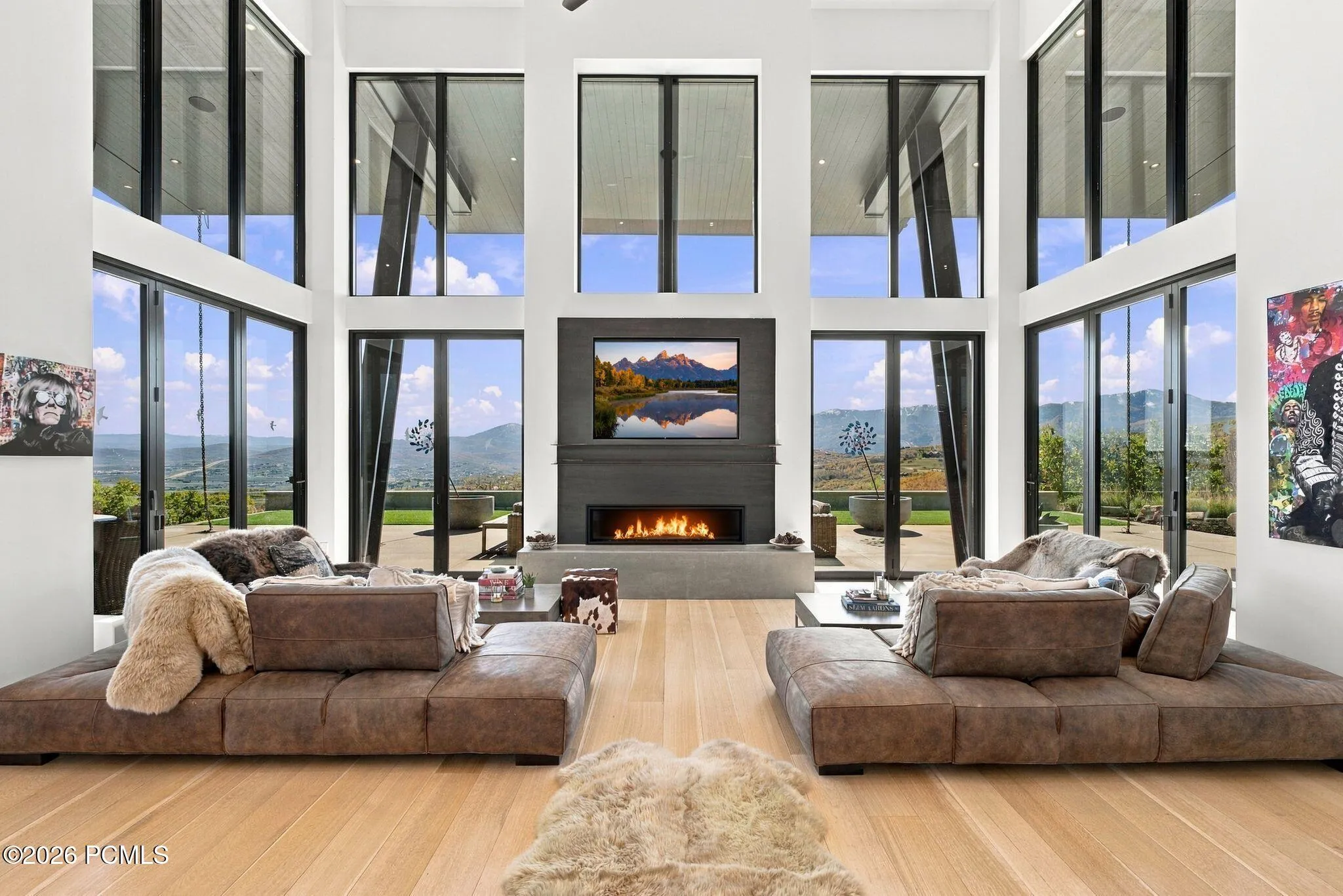 Double-height ceilings with floor-to-ceiling windows, linear fireplace with custom surround, wood-finish flooring, and pass through views toward Park City