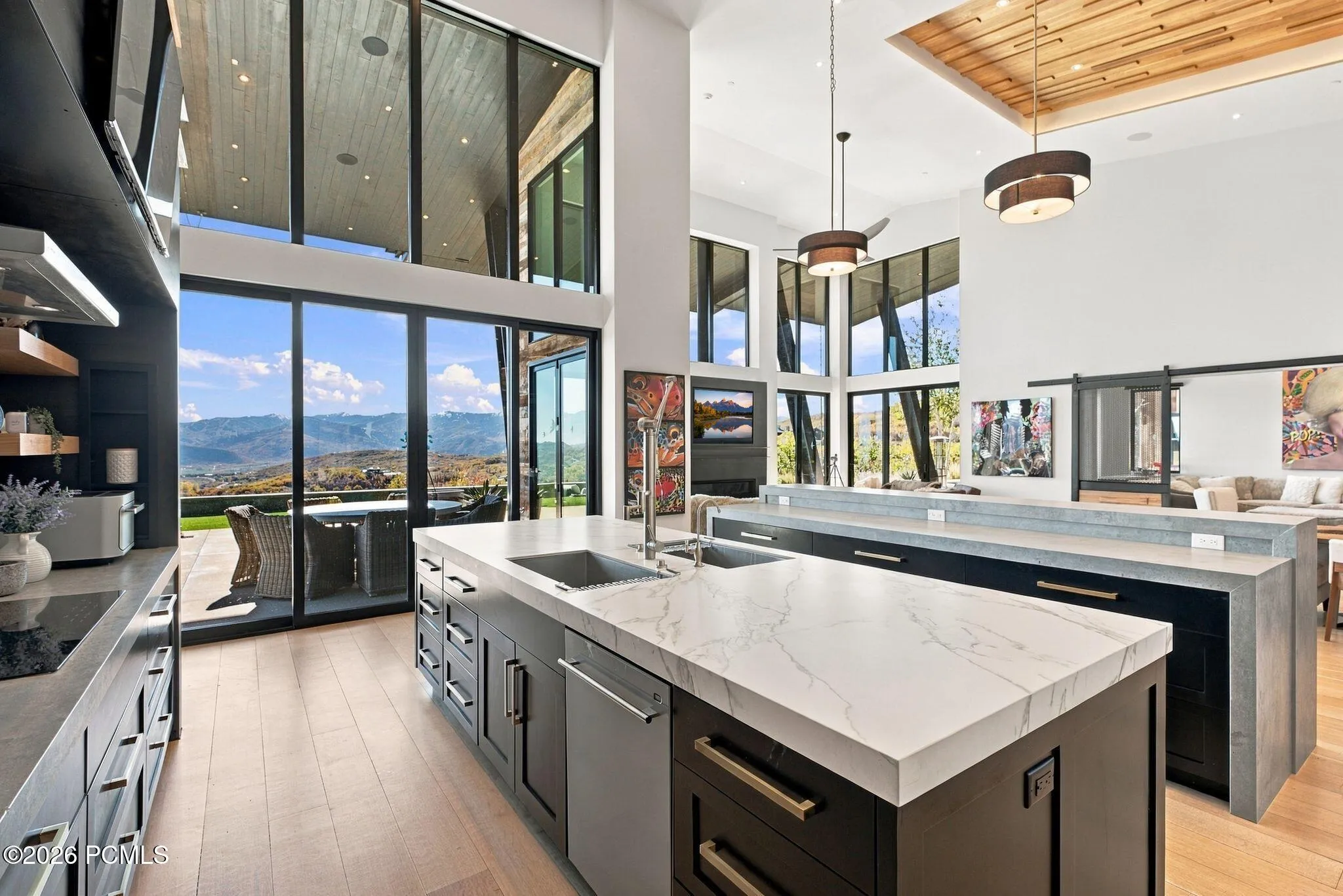 Expansive interior featuring floor-to-ceiling windows, wood-finish flooring, a kitchen island with stone countertops, a coffered wood-paneled ceiling, and sliding glass doors