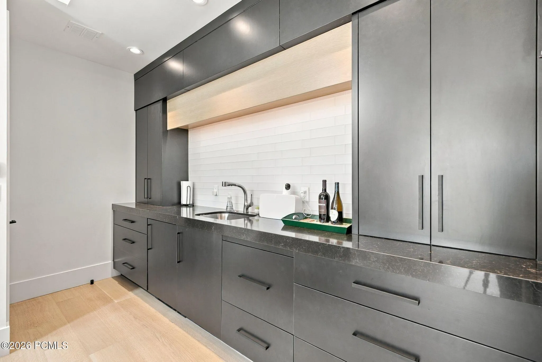 Custom built-in wetbar in guest quarters with integrated under-cabinet lighting, a white horizontal tile backsplash, quartz countertops