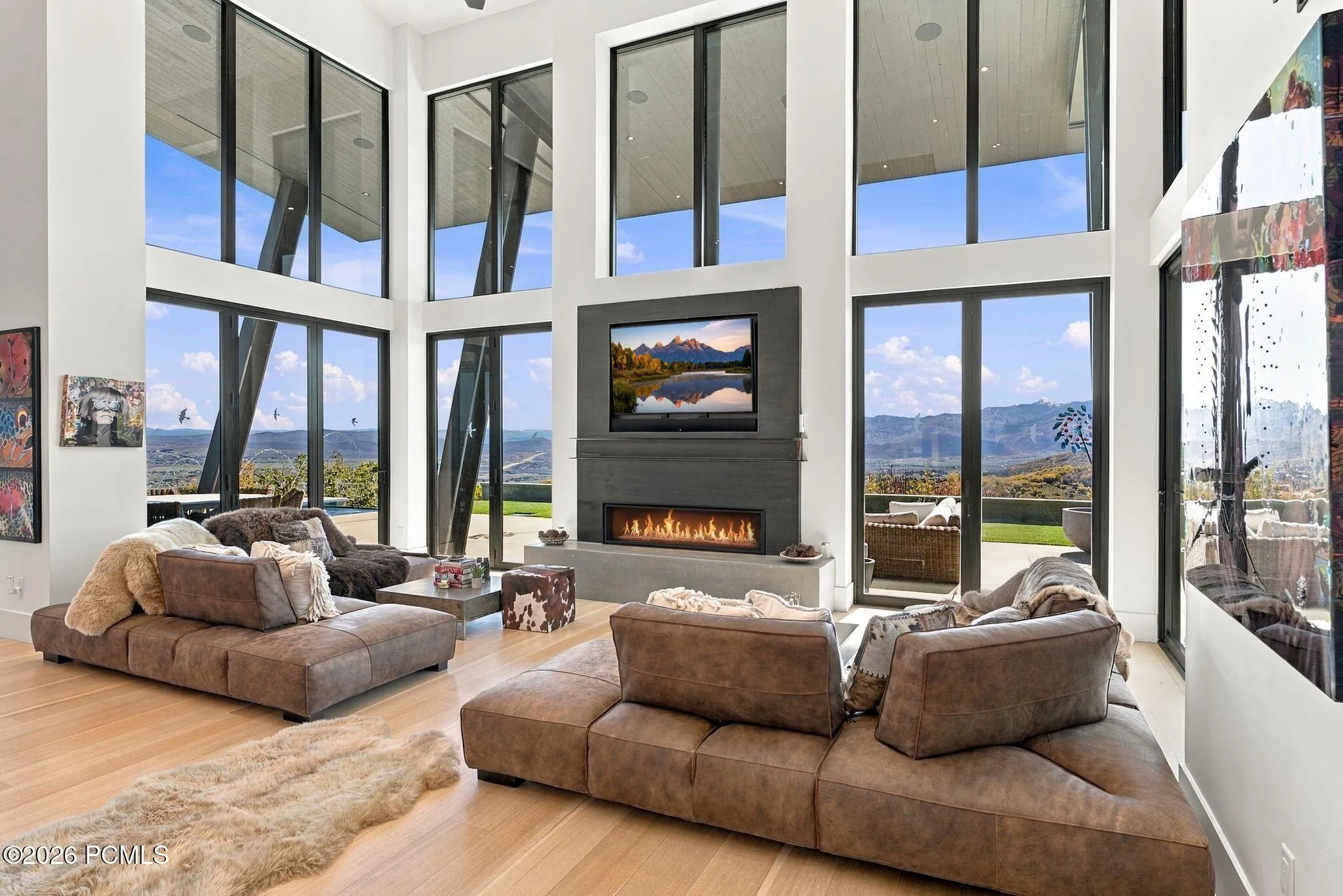 Double-height ceilings with floor-to-ceiling windows, linear fireplace with custom surround, wood-finish flooring, and pass through views toward Park City