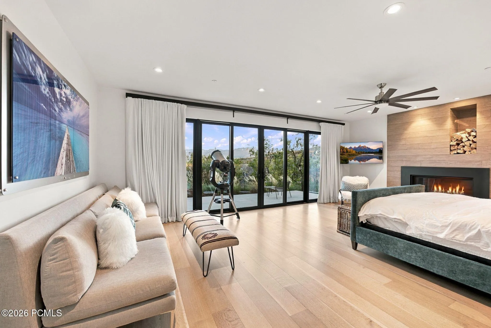 Primary bedroom featuring views toward Park City, wide-plank wood-finish flooring, floor-to-ceiling sliding glass doors, horizontal wood-paneled accent wall, built-in gas fireplace