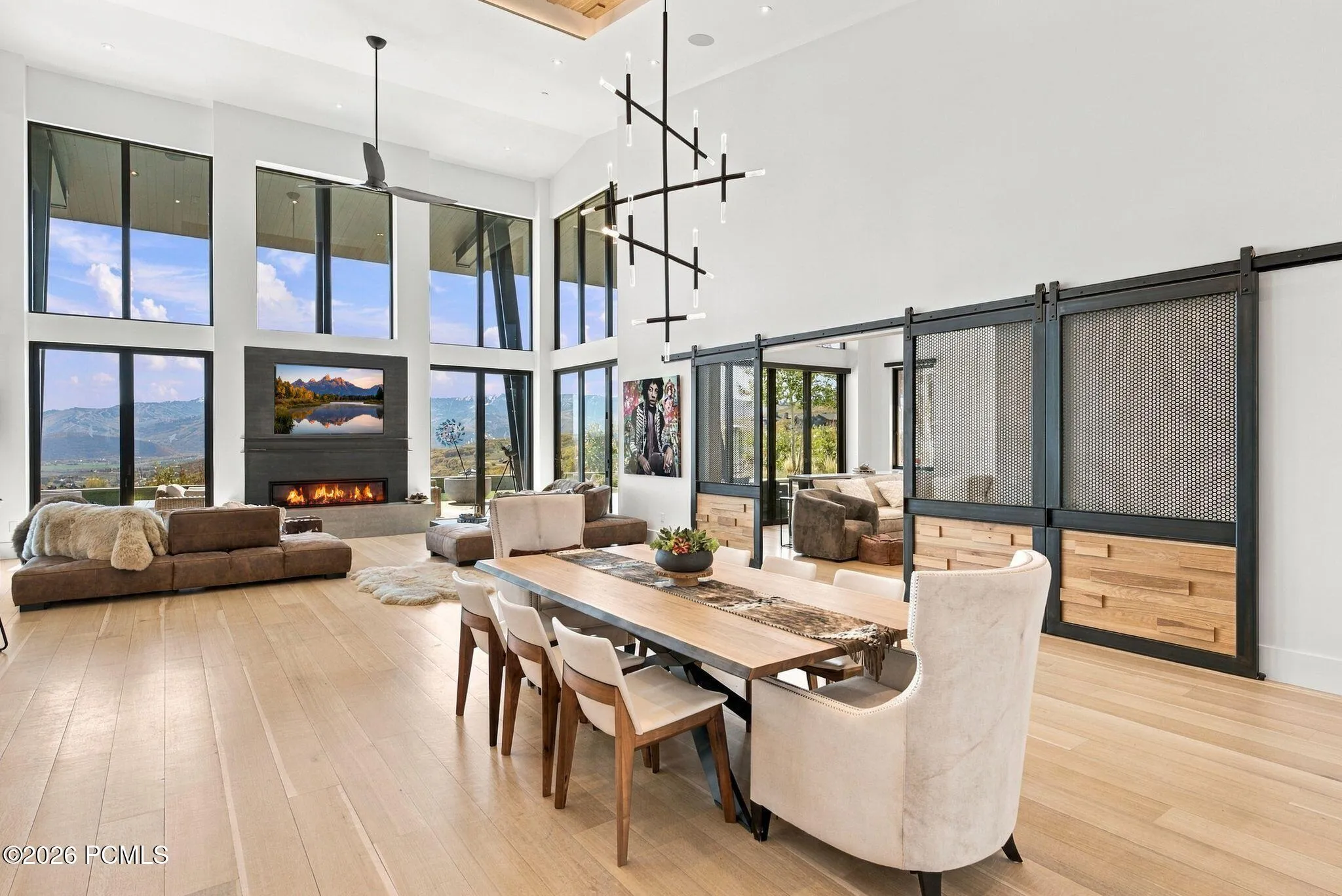 Double-height ceilings with floor-to-ceiling windows, linear fireplace with custom surround, wood-finish flooring, and pass through views toward Park City