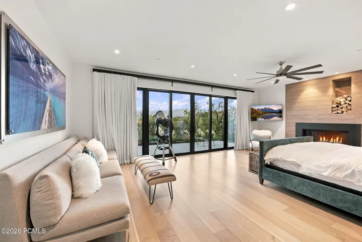 Primary bedroom featuring views toward Park City, wide-plank wood-finish flooring, floor-to-ceiling sliding glass doors, horizontal wood-paneled accent wall, built-in gas fireplace