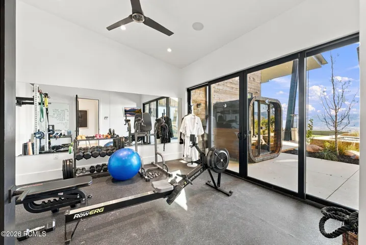 Gym with vaulted ceilings wall-to-wall mirrors, large glass sliding doors opening to an exterior concrete patio with inspiring views and direct sauna access.