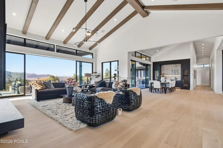 The living, dining & kitchen spaces unfold within the spectacular great room, where uninterrupted sightlines & effortless transitions create a remarkable sense of openness. Soaring vaulted ceilings adorned with richly textured wood beams, European white oak flooring & a commanding floor-to-ceiling metal fireplace establish a sophisticated balance of warmth & contemporary refinement, while a magnificent gallery of glass frames sweeping Deer Valley vistas throughout the interconnected spaces.