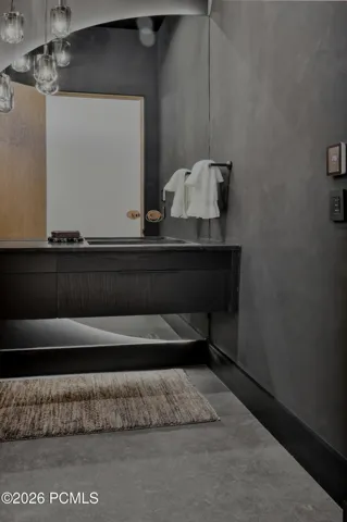 A dramatic toned powder room makes a memorable impression with its chic, dark palette & luminous detailing. An illuminated mirror extends below the vanity cabinetry, casting a soft, ambient glow that accentuates the room’s distinctive character & contemporary elegance.