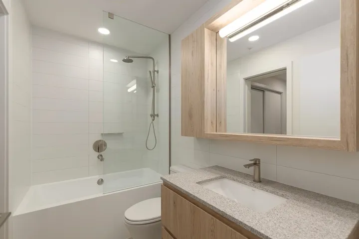 Bathroom featuring a frameless glass shower panel, white subway tile surround, integrated bathtub, wood-finish vanity with a built-in sink, and a mirrored medicine cabinet