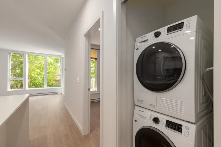 In-unit stackable washer and dryer appliances, light wood-finish flooring, and expansive windows