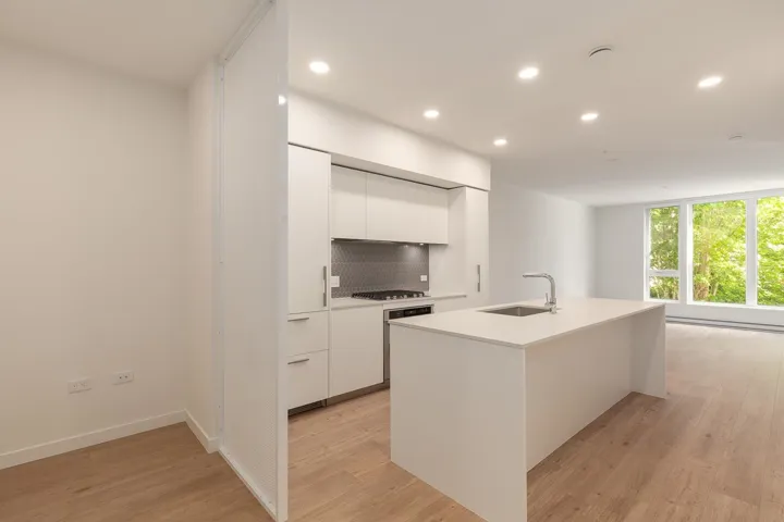Modern kitchen featuring a white center island with an undermount sink, stainless steel faucet, white cabinetry, and a gray hexagonal tile backsplash