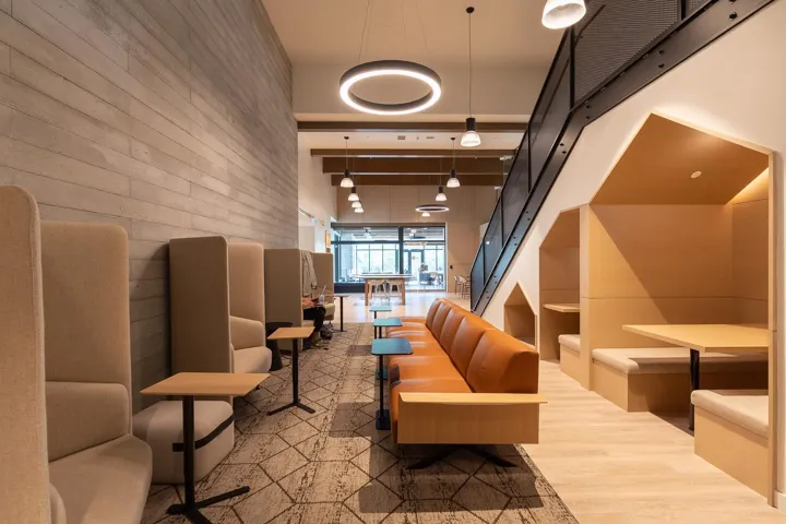 Contemporary lounge area with varied seating options, including high-back upholstered chairs, a long leather sofa with wood-finish armrests, and built-in booth seating under a black metal staircase