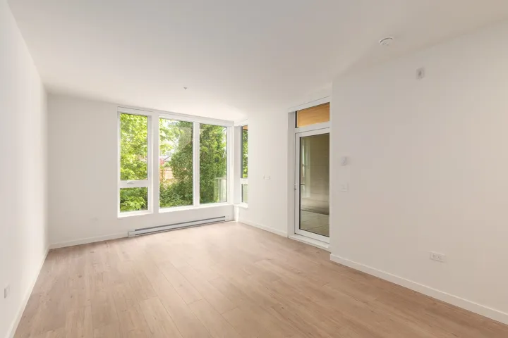 Bright living space featuring expansive windows, wood-finish flooring, crisp white walls, and a glass-paneled door