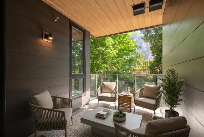 Covered outdoor patio featuring wood-finish ceiling, dark horizontal siding, recessed lighting, and a glass-paneled railing