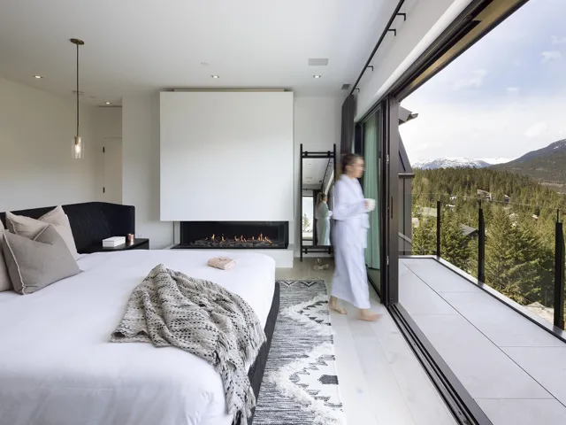 Bedroom featuring a warm lit fireplace, light wood finished floors, a mountain view, and a wooded view