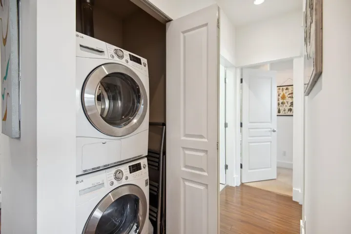 Washroom featuring stacked washer and clothes dryer, wood finished floors, and laundry area