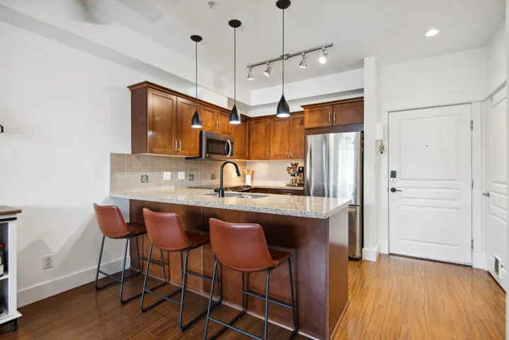Kitchen featuring dark wood-type flooring, a sink, backsplash, appliances with stainless steel finishes, and a peninsula