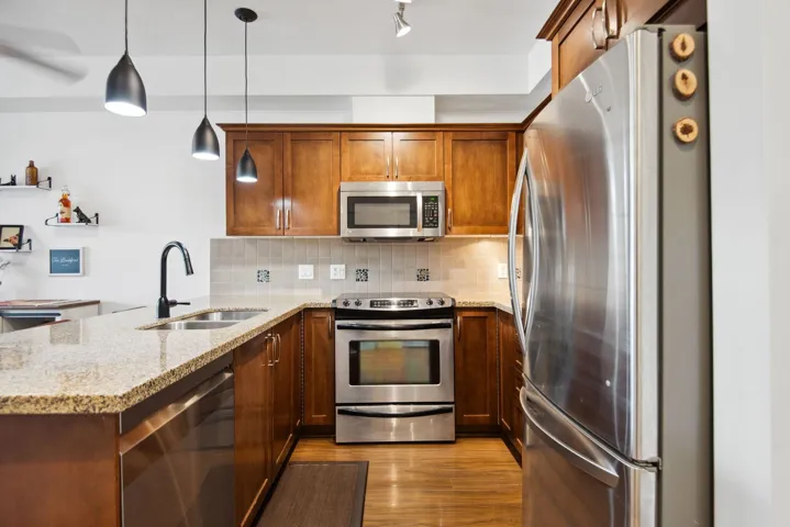 Kitchen featuring light wood-style flooring, a sink, stainless steel appliances, a peninsula, and decorative backsplash