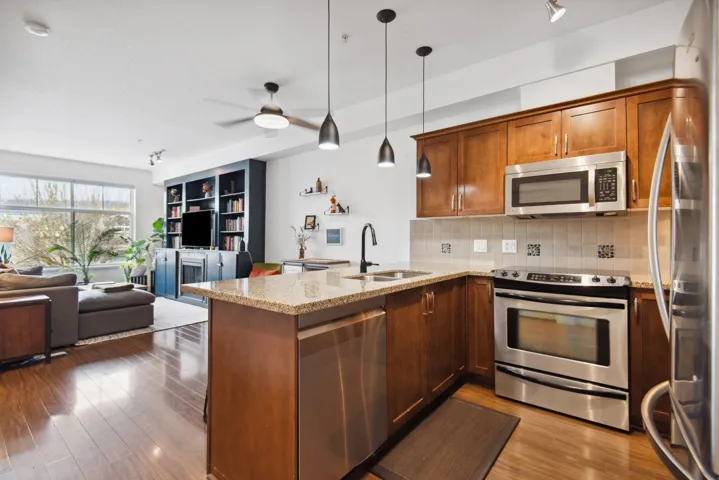 Kitchen featuring wood finished floors, a peninsula, a sink, appliances with stainless steel finishes, and open floor plan