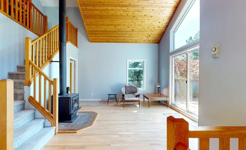 Living area featuring high vaulted ceiling, a wood stove, stairway, wood finished floors, and wooden ceiling