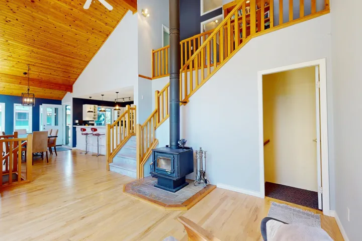 Living room with high vaulted ceiling, wood finished floors, stairway, a wood stove, and wooden ceiling