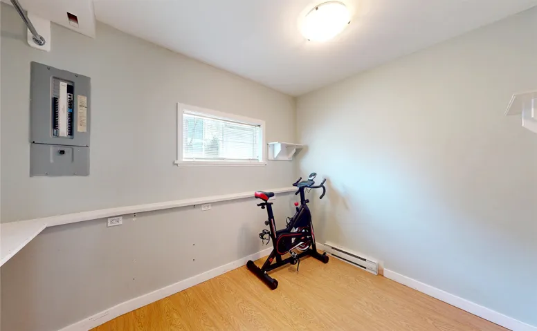 Workout room with a baseboard radiator, light wood-style flooring, and electric panel