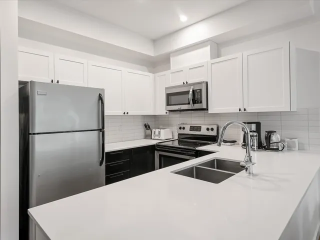 Kitchen with white cabinetry, a sink, stainless steel appliances, light countertops, and backsplash